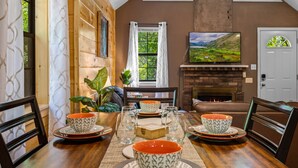 A cozy dining area with a wooden table set for four, surrounded by chairs. A fireplace is visible in the background, and a painting hangs on the wall. - Hot Tub, Game Room, Pool Table, Fireplace | Minutes to Pigeon Forge (Sevierville)