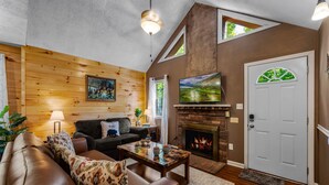A cozy living room with a fireplace, wooden walls, a sofa, and a television. - Hot Tub, Game Room, Pool Table, Fireplace | Minutes to Pigeon Forge (Sevierville)