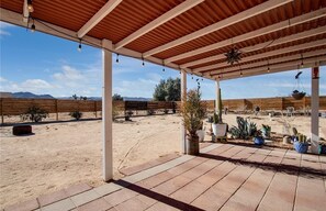 Un patio couvert offrant une vue sur un paysage désertique, agrémenté de plantes en pot et d’une clôture en bois.