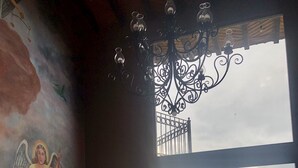 A room with a mural of an angel, a wooden bench, a glass table, and a balcony with a view of a body of water.