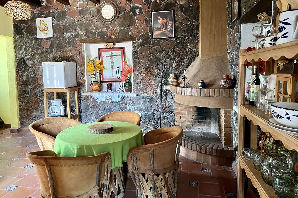 A rustic interior with a stone wall, a fireplace, and a dining area with a green tablecloth.