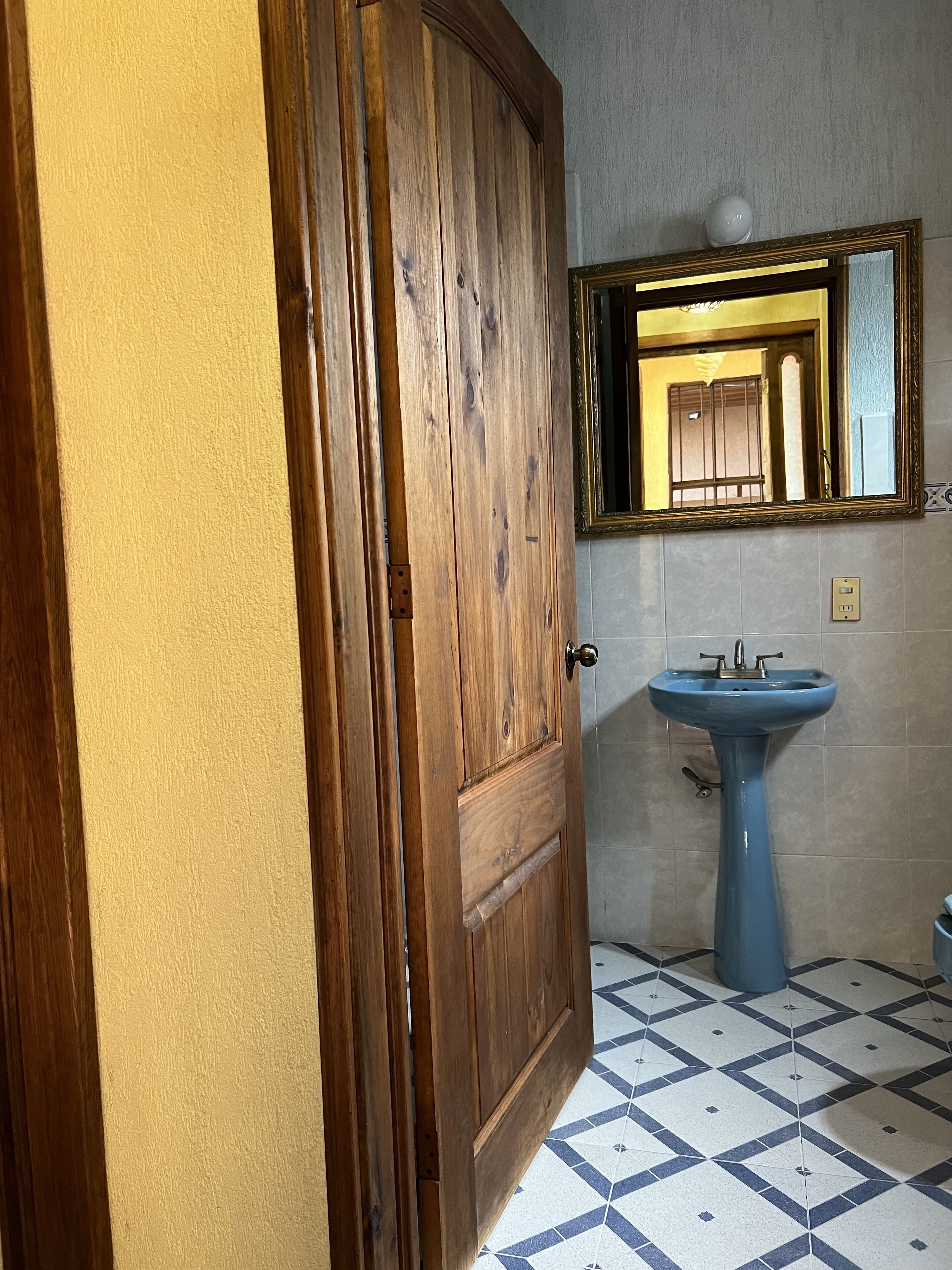 A bathroom with a wooden door, a blue sink, and a tiled floor.