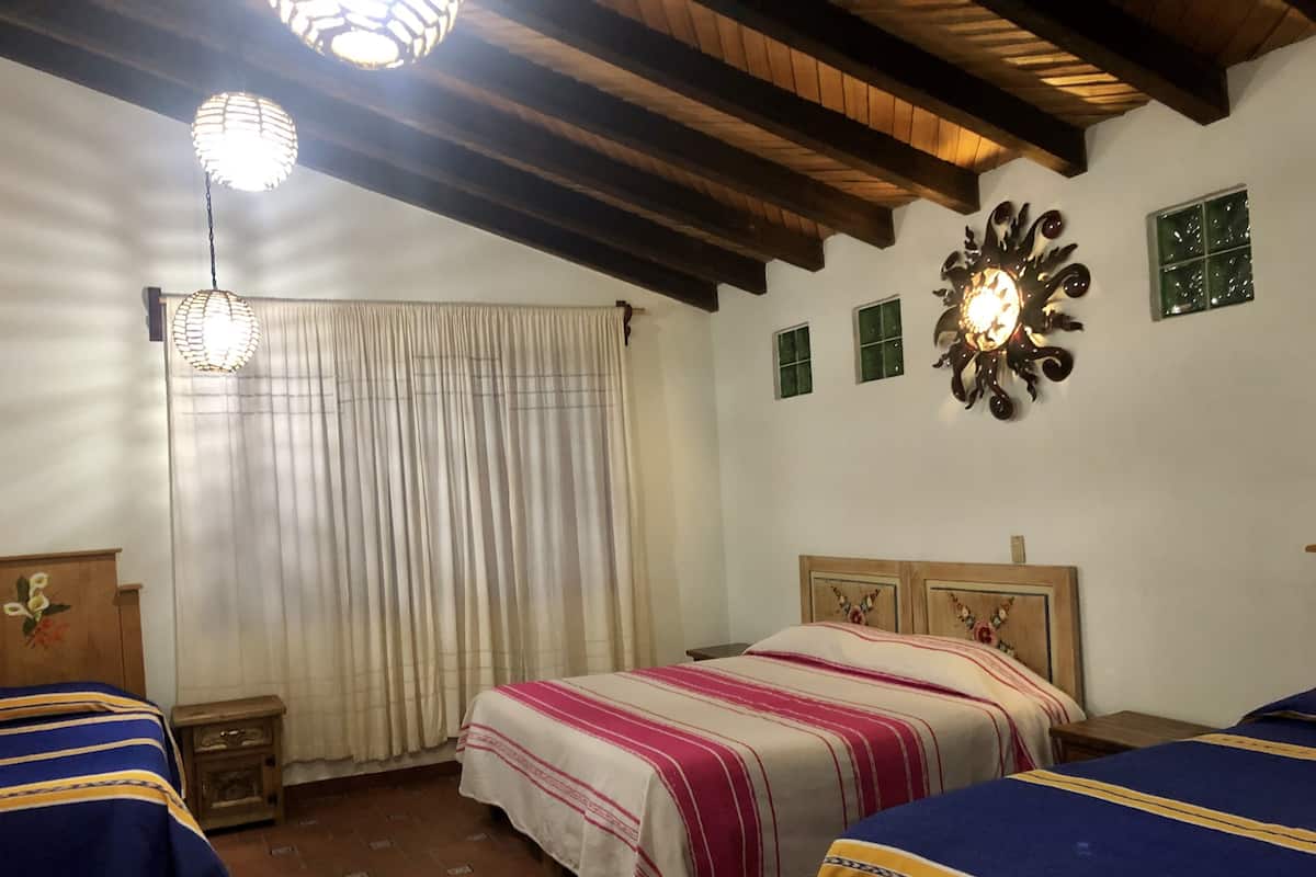 A bedroom with two beds, a wooden ceiling, a decorative wall piece, and a window with curtains.