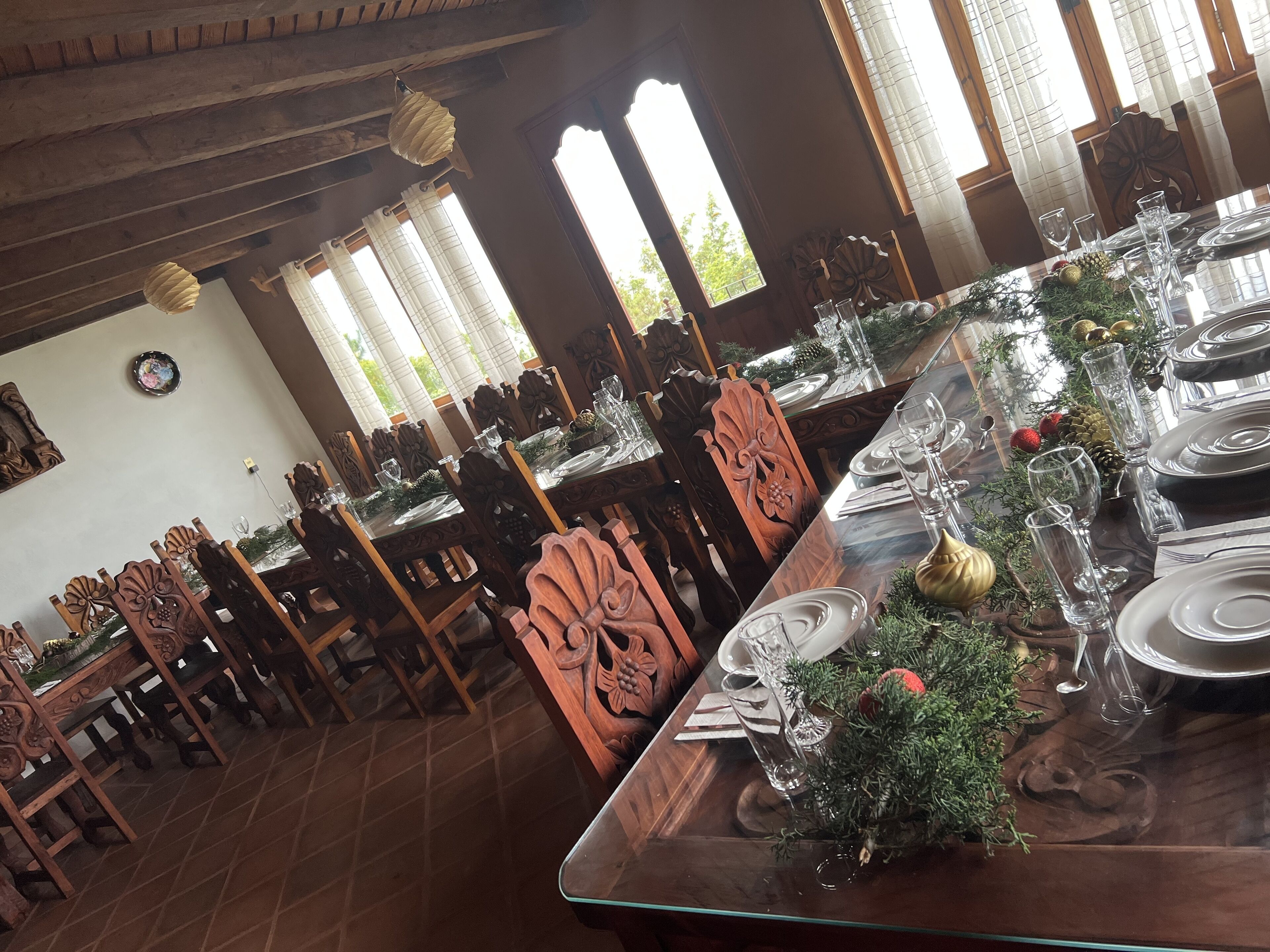 Un comedor con sillas y mesas de madera, decorado con follaje y cristalería transparente.
