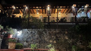 A stone wall with potted plants and a wooden pergola with hanging lights.