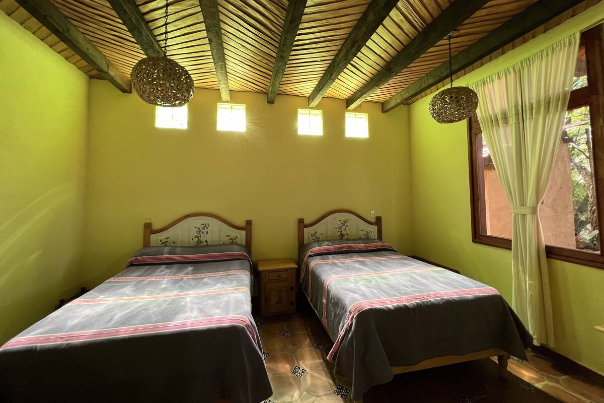 A room with two beds, a wooden ceiling, and a window with curtains.