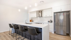 Une cuisine moderne dotée d’un îlot central, de tabourets de bar, d’un réfrigérateur en acier inoxydable et de meubles de cuisine blancs.