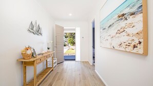 Un couloir avec une console en bois, un tableau encadré représentant une plage et une porte donnant sur l’extérieur.