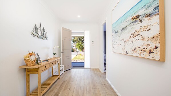 A hallway with a wooden console table, a framed picture of a beach, and a door leading outside.