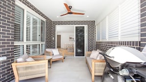 Une chambre moderne avec un mur en briques, un ventilateur de plafond, une porte-fenêtre coulissante donnant sur un coin repas et une station de recharge pour trottinette électrique.
