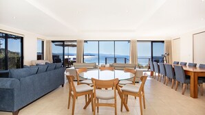Un salón amplio con una mesa redonda de vidrio rodeada de sillas de madera, un sofá azul y una zona de comedor con una mesa y sillas de madera.