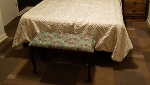 Une chambre à coucher avec un lit, un banc, une table de chevet en bois et un mur de couleur sombre.