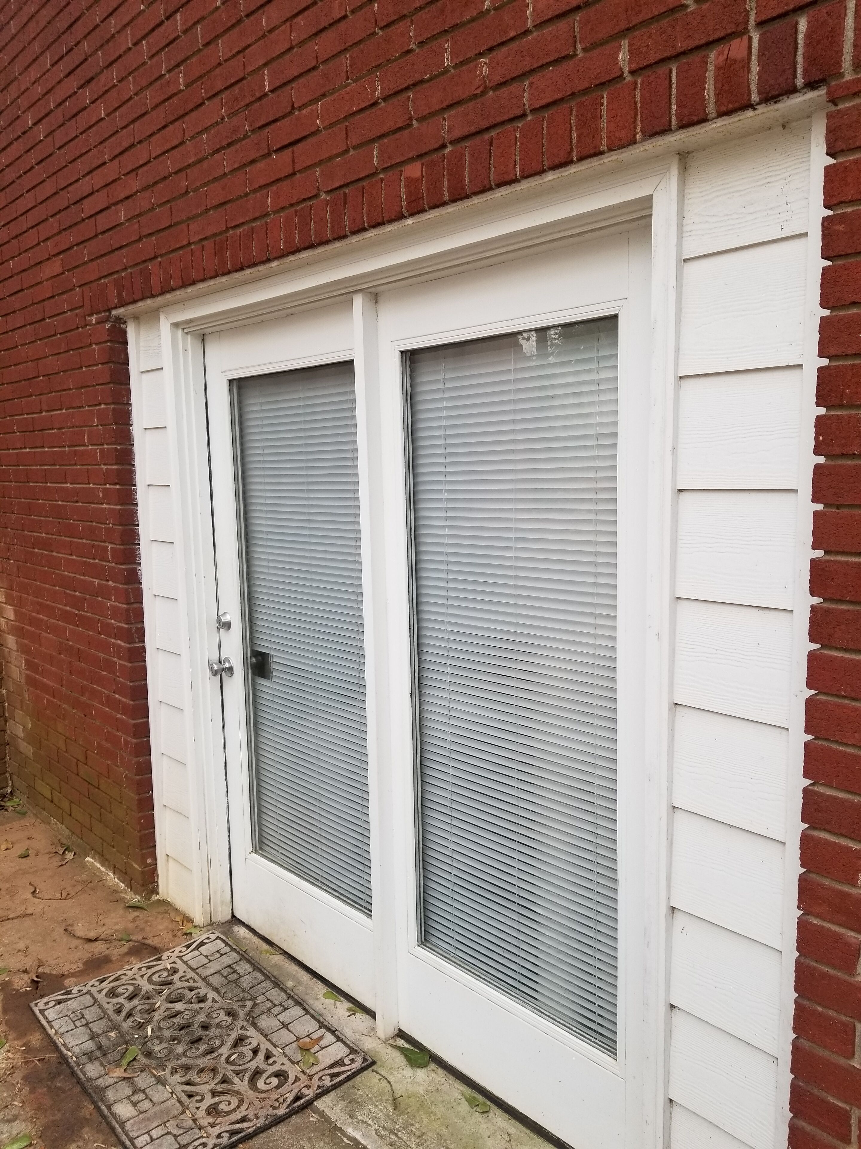 Une porte à deux battants avec un grillage métallique, une façade blanche et un mur en briques.
