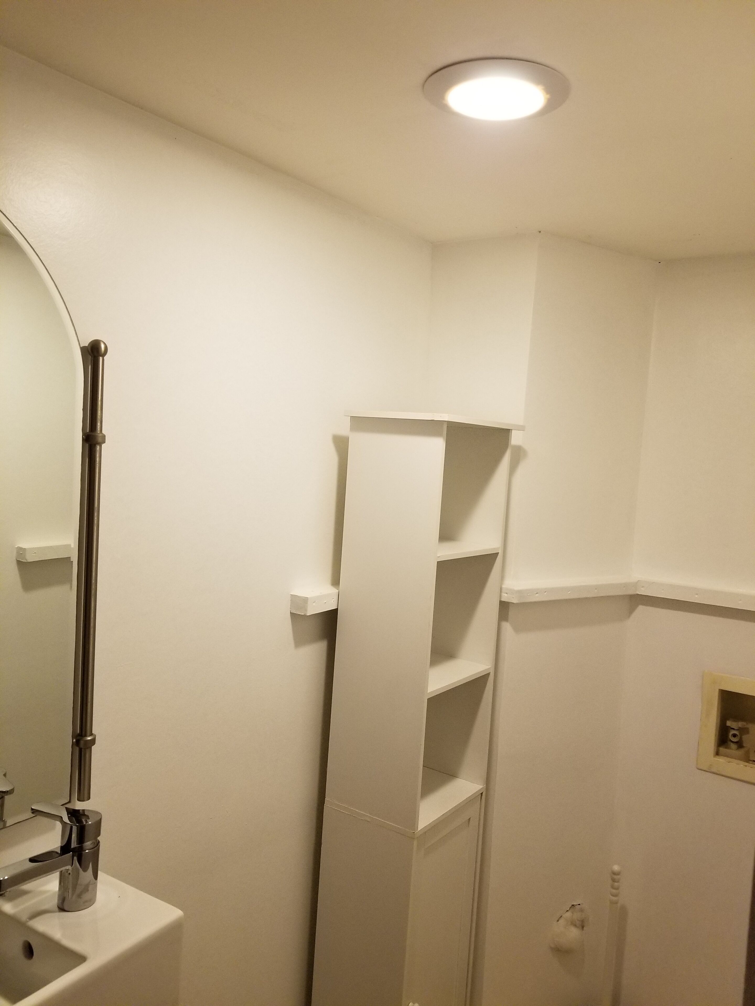Une salle de bain avec un lavabo blanc, un miroir, une étagère et des toilettes.