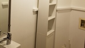 Une salle de bain avec un lavabo blanc, un miroir, une étagère et des toilettes.