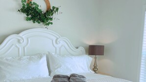 Una cama bien hecha con una colcha estampada, una pila de toallas dobladas, una lámpara de noche y una planta colgante en la pared.