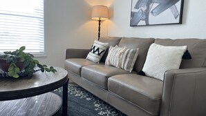 Una sala de estar con un sofá color beige, una mesa de centro redonda, una planta en maceta y una alfombra estampada.