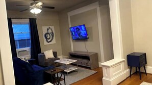 A living room with a TV, a ceiling fan, a sofa, and a coffee table. - Highland Park Place: Historic Two Bedroom Apt! (Roanoke)