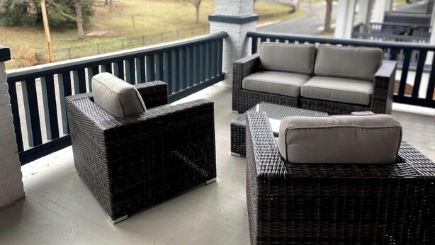 A covered outdoor seating area with wicker furniture and a view of a residential neighborhood. - Highland Park Place: Historic Two Bedroom Apt! (Roanoke)
