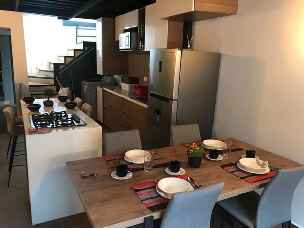 Une cuisine moderne avec un coin repas, des appareils électroménagers en acier inoxydable et un escalier menant à un autre niveau.