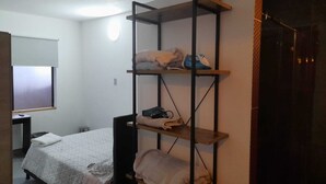 A bedroom with a bunk bed, a desk, and a shelving unit with folded clothes and a blue iron.