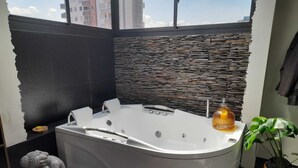 A modern bathroom with a freestanding bathtub, stone wall, and a view of buildings.