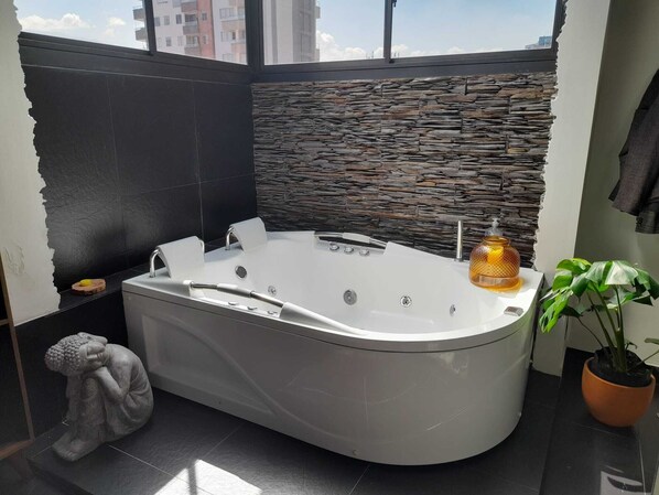 A modern bathroom with a freestanding bathtub, stone wall, and a view of buildings. - Beautiful Modern Apartment, Very Safe. Jacuzzi, Bbq, Terrace. 4bed/4bath (Medellín)