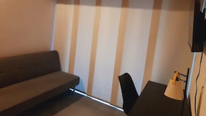 A room with a sofa, a chair, a desk, and a TV mounted on the wall.