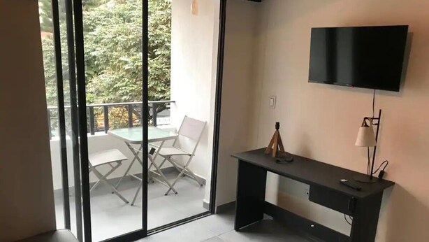 A room with a desk, a flat-screen TV, and a sliding glass door leading to an outdoor area with a table and chairs.