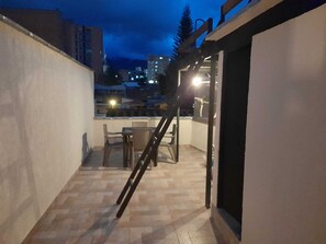 A small balcony with a table and chairs, a wooden ladder, and a view of the city at dusk. - Beautiful Modern Apartment, Very Safe. Jacuzzi, Bbq, Terrace. 4bed/4bath (Medellín)