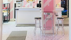 Isbutik med et interiør i pink og hvid, en disk med barstole og en menutavle, der viser priser for isvafler, kuverter og milkshakes.