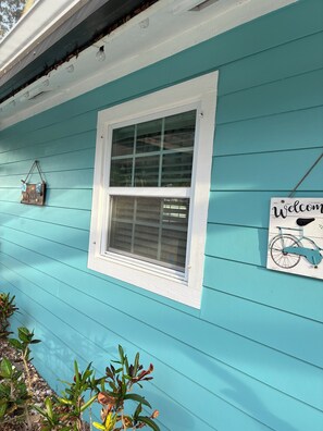 A turquoise house with a white window, a welcome sign with a bicycle, and a hanging sign with a beach theme.