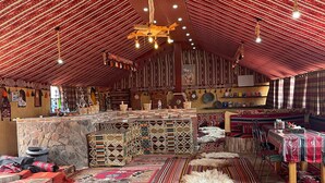 A traditional interior with patterned carpets, a stone counter, and a central seating area. - Khaleds Camp (Wadi Rum)