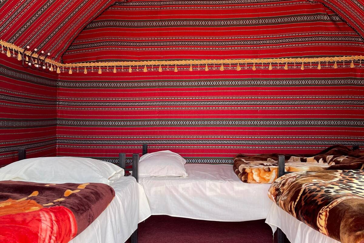 Une pièce en forme de tente, avec deux lits, des murs décorés de motifs rouges et une moquette rouge.