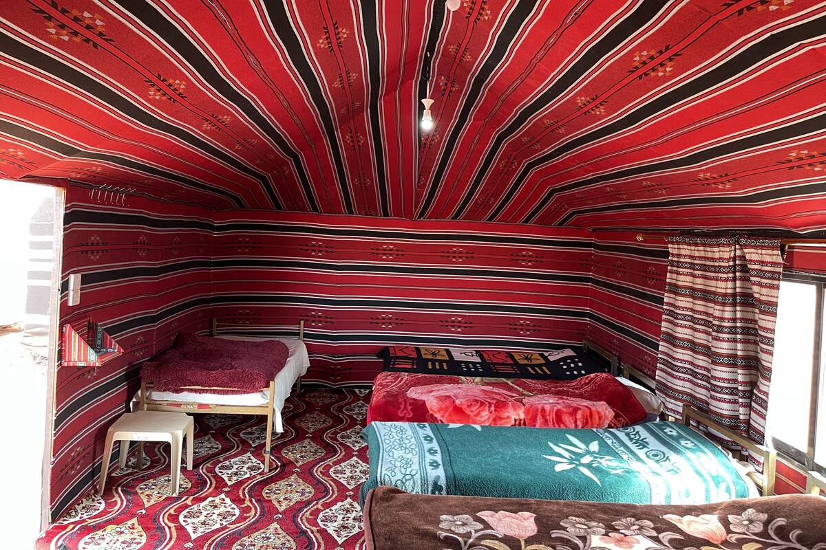Une pièce avec un plafond en pente et des murs à motifs, un lit recouvert d’une couverture rouge et blanche, un petit tabouret et un tapis à motifs.