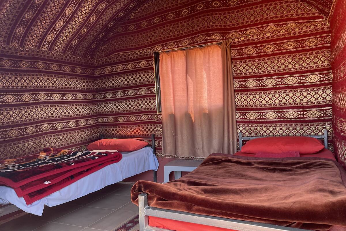 Une chambre avec deux lits, des murs à motifs et un rideau.