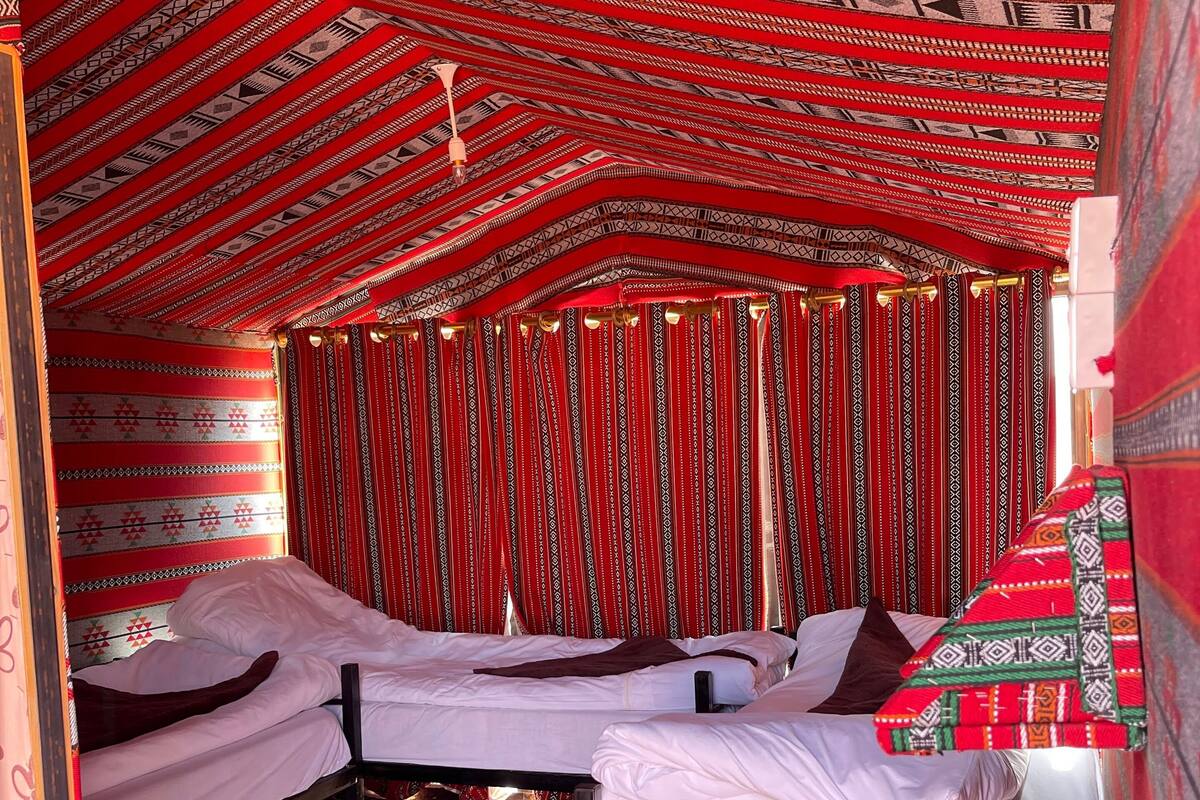 Une petite chambre accueillante, avec deux lits simples, une moquette à motifs et un rideau rayé de rouge et de blanc.