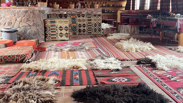 A spacious room with a high ceiling, patterned rugs, and a stone wall. - Khaleds Camp (Wadi Rum)
