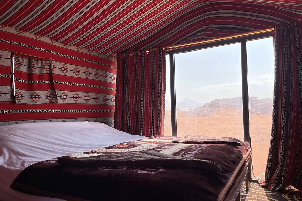 Une chambre avec un lit, des rideaux à motifs et une vue sur un paysage désertique.