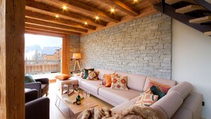 A cozy living room with a stone wall, wooden ceiling beams, and a sofa with colorful cushions. - Bain à Remous+Terrasse Panoramique! Chalet Raffiné (Les Deux Alpes)