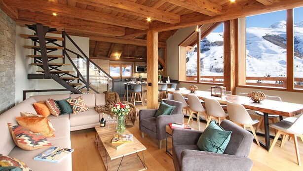 A cozy interior with a wooden staircase, a dining area, and large windows offering a snowy mountain view. - Bain à Remous+Terrasse Panoramique! Chalet Raffiné (Les Deux Alpes)