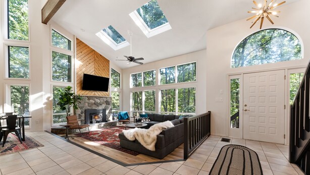 A spacious living room with a fireplace, large windows, and a ceiling fan. - Modern Poconos Game House! Hot Tub, Fire Pit (East Stroudsburg)