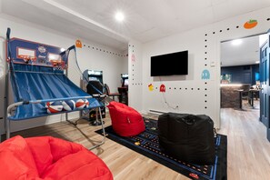 A room with a blue and red play area, including a slide and basketball hoop, a flat-screen TV mounted on the wall, and a red bean bag chair. - Modern Poconos Game House! Hot Tub, Fire Pit (East Stroudsburg)