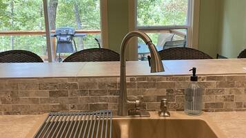 A kitchen with a stainless steel sink, a built-in grill, and a window overlooking a deck.
