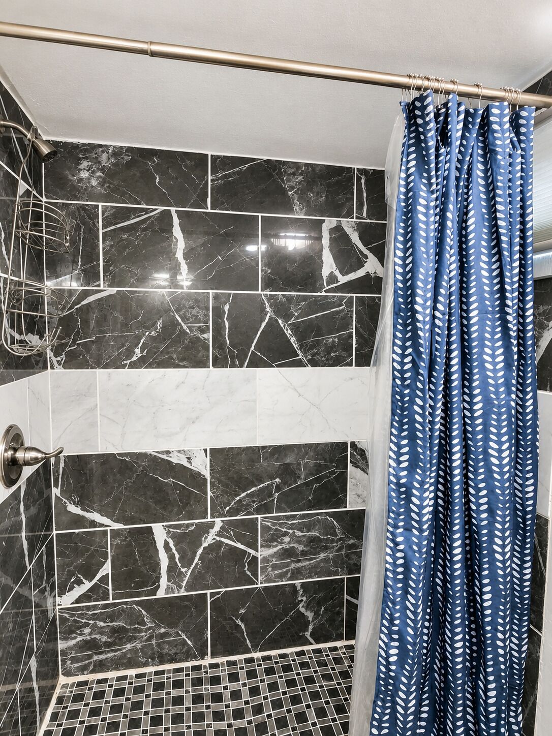 Une salle de bain avec des carreaux de marbre noir et blanc, un rideau de douche orné d’un motif de feuilles et une pomme de douche en métal.