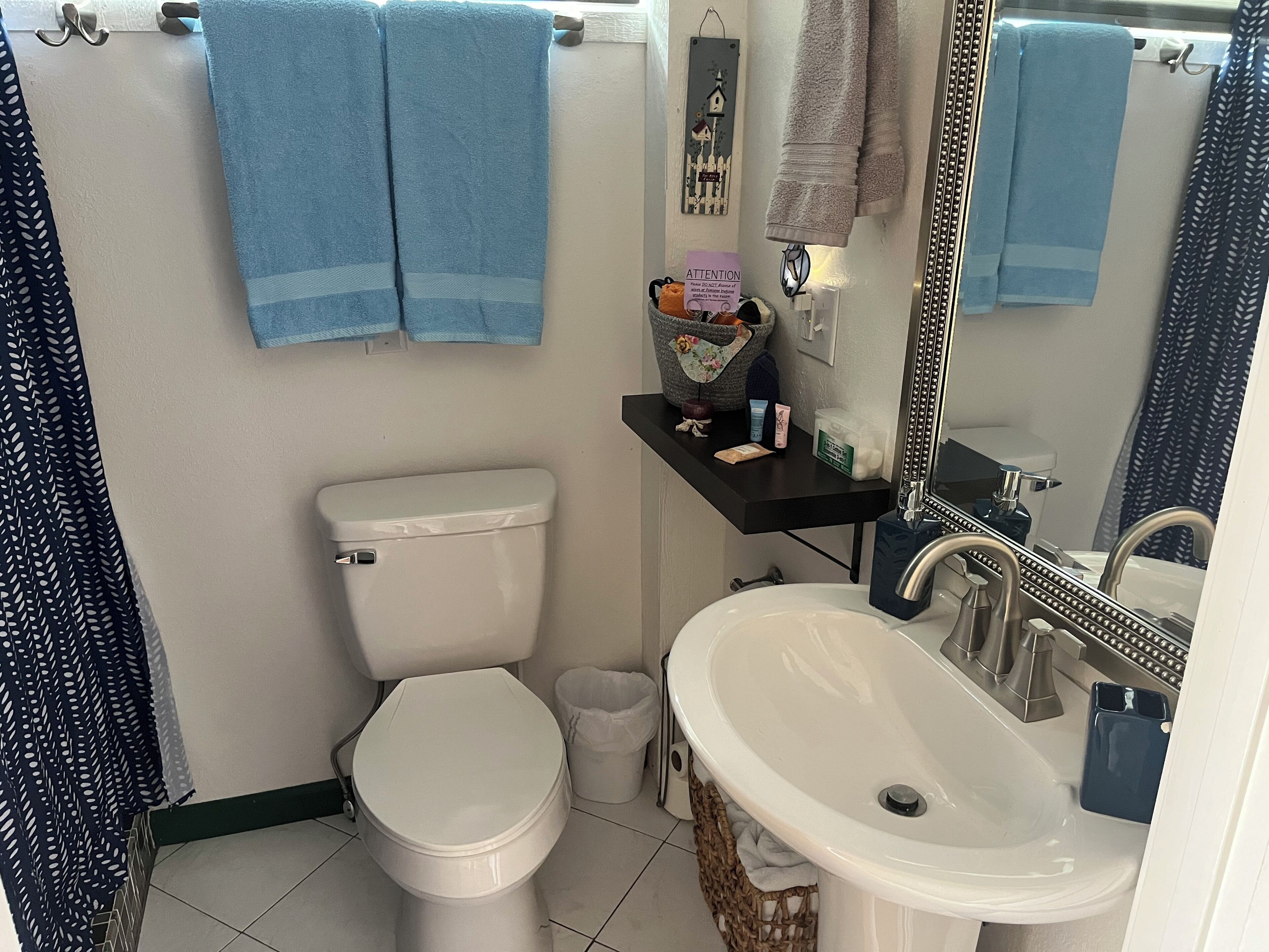 Une salle de bain équipée de toilettes, d’un lavabo et d’une étagère où sont rangés les articles de toilette.