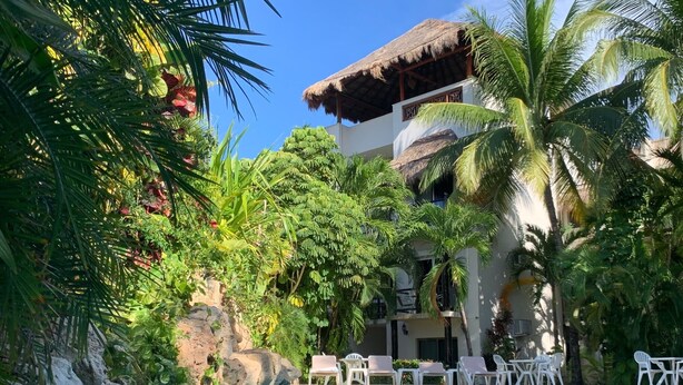 A pool surrounded by lush greenery, a thatched-roof building, and white lounge chairs. - Casa De Namaste- Relaxing 1 Br Condo near Playa's best Beaches & 5th Ave! (Playa del Carmen)