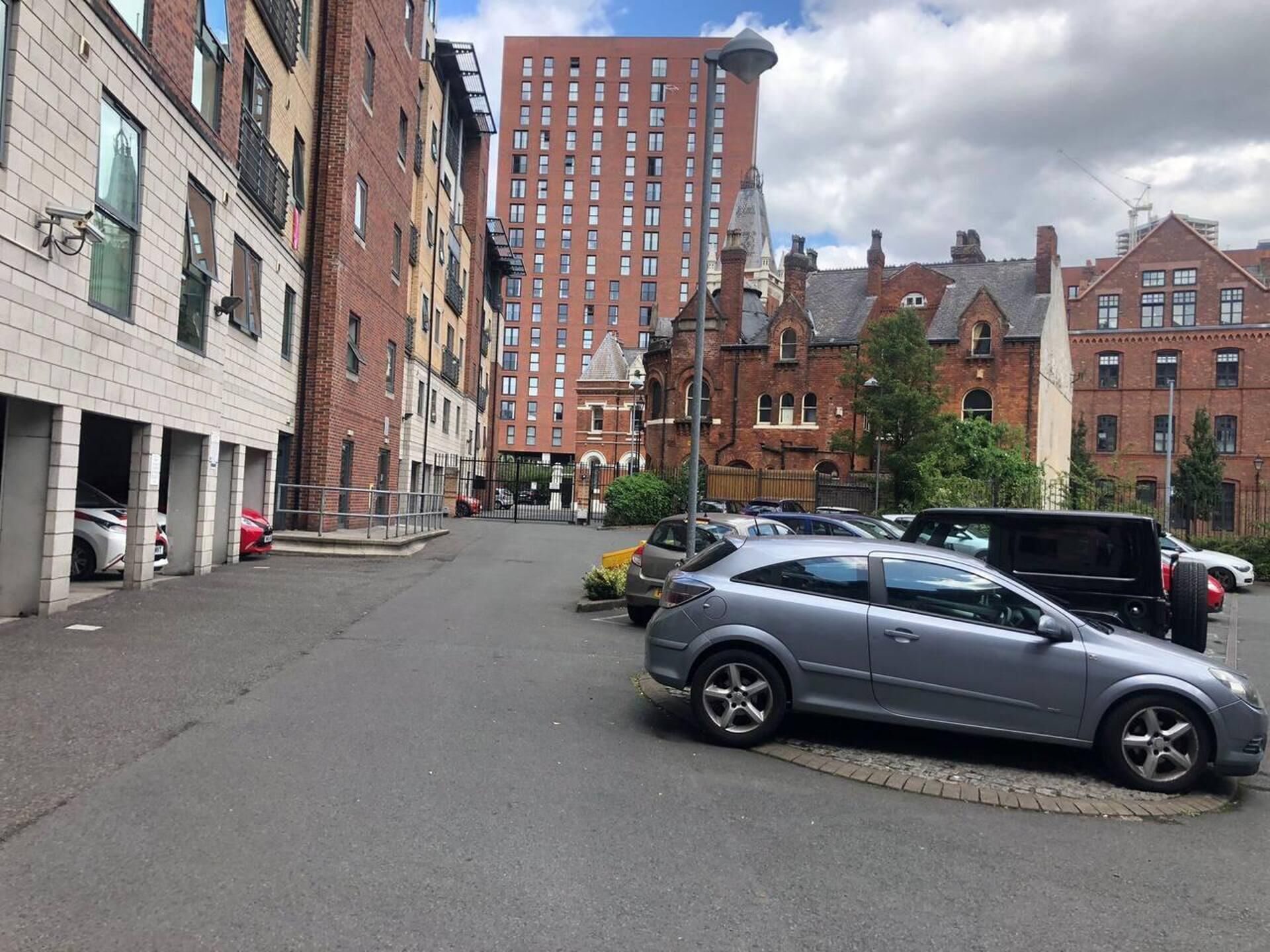 A parking lot with cars, a building with a red brick facade, and a taller red building in the background.