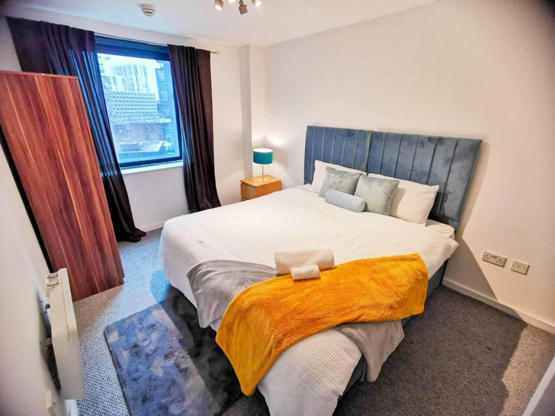 Une chambre d’hôtel avec un grand lit, une table de chevet avec une lampe, une fenêtre avec des rideaux et une vue sur la ville.