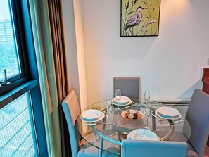 A dining area with a round glass table, four chairs, and a painting on the wall.